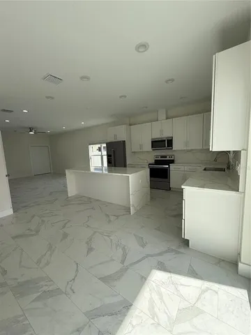 a large white kitchen with kitchen island a sink a stove a oven with a dining table and a large window