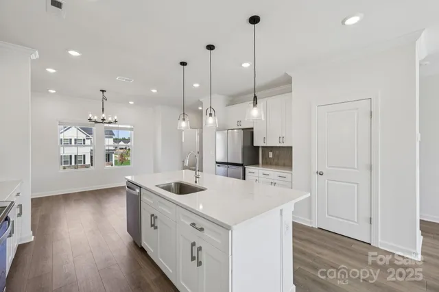 a kitchen with stainless steel appliances a stove a sink a refrigerator and white cabinets with wooden floor
