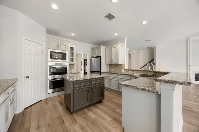 a kitchen with stainless steel appliances granite countertop a stove top oven a sink dishwasher a refrigerator and a oven with wooden floor