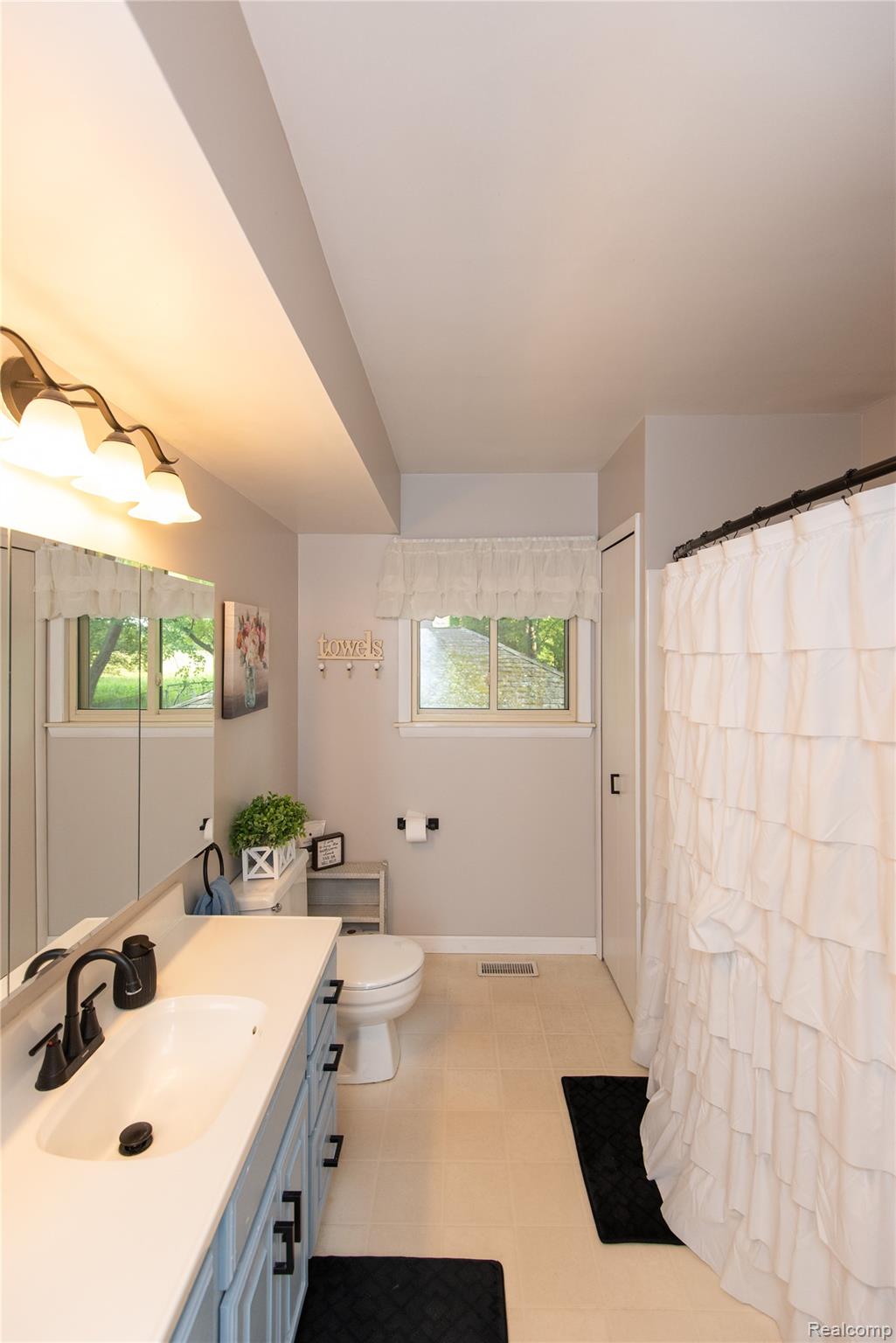 4395 Regency Road Swartz Creek, MI 48473 - Photo 42 of 67 Bathroom featuring a vanity with a white countertop and dark-toned faucet, light-toned floor tiling, and a window with a sheer valance