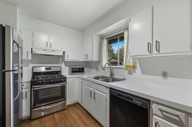 a kitchen with cabinets stainless steel appliances a sink and wooden floor