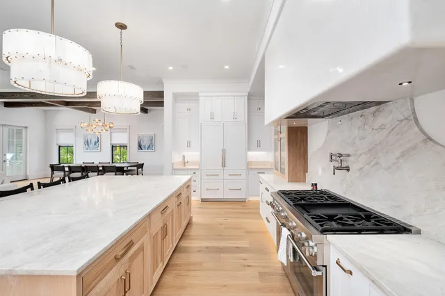 a large kitchen with kitchen island a stove a sink a oven and a dining table with wooden floor