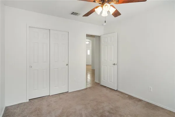 an empty room with a chandelier fan and closet area