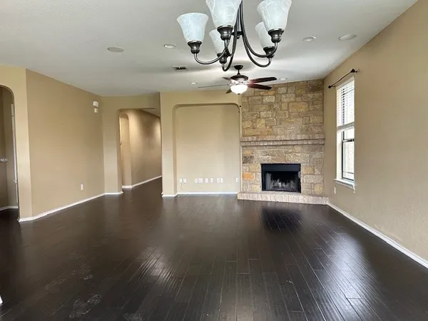 an empty room with wooden floor chandelier fan and windows