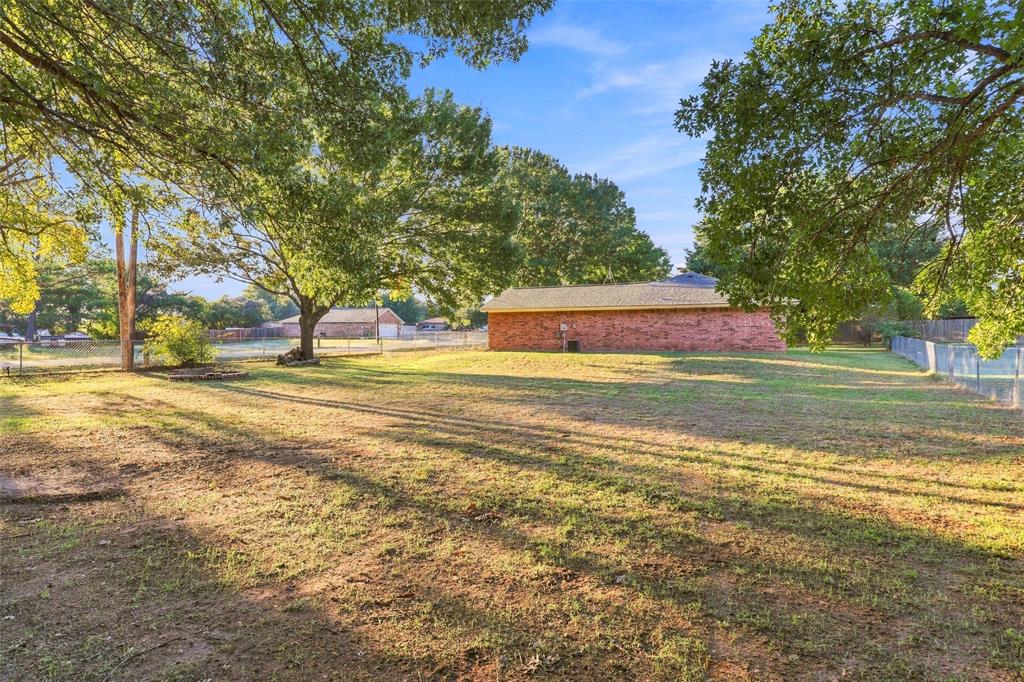 304 Sage Trail Springtown, TX 76082 - Photo 26 of 33 Rear Yard – Generous outdoor space with mature trees and views of the home's brick exterior.