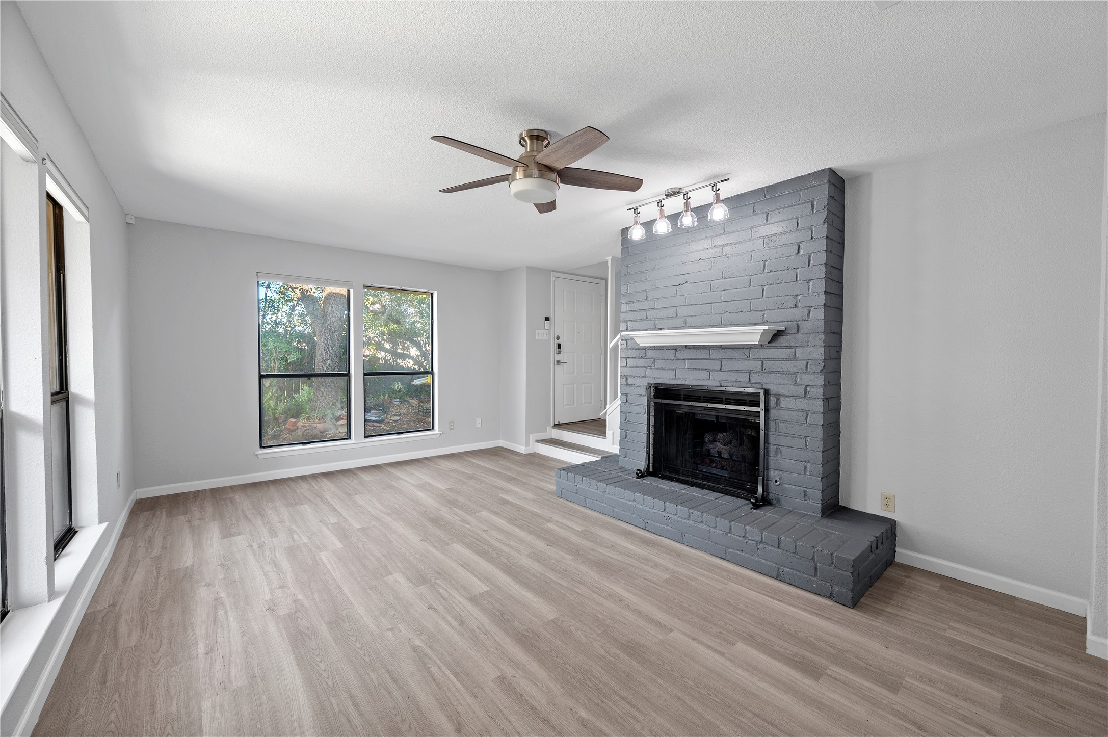 11301 Jollyville Road, Unit B3 Austin, TX 78759 - Photo 8 of 23 Unfurnished living room featuring a ceiling fan, a brick fireplace, and light wood-style flooring