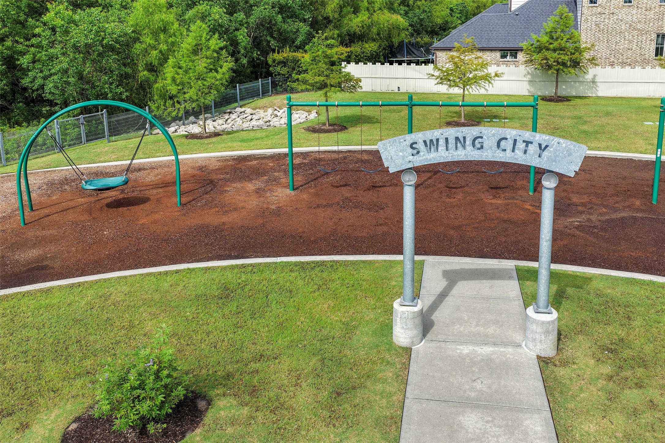 10603 Whitejacket Conroe, TX 77385 - Photo 35 of 42 This photo features a playground named "Swing City" with swings and a basket swing set in a grassy area, surrounded by trees and a nearby house. Ideal for families seeking nearby recreational spaces.