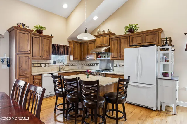 a kitchen with granite countertop a refrigerator a stove a sink and white cabinets with wooden floor