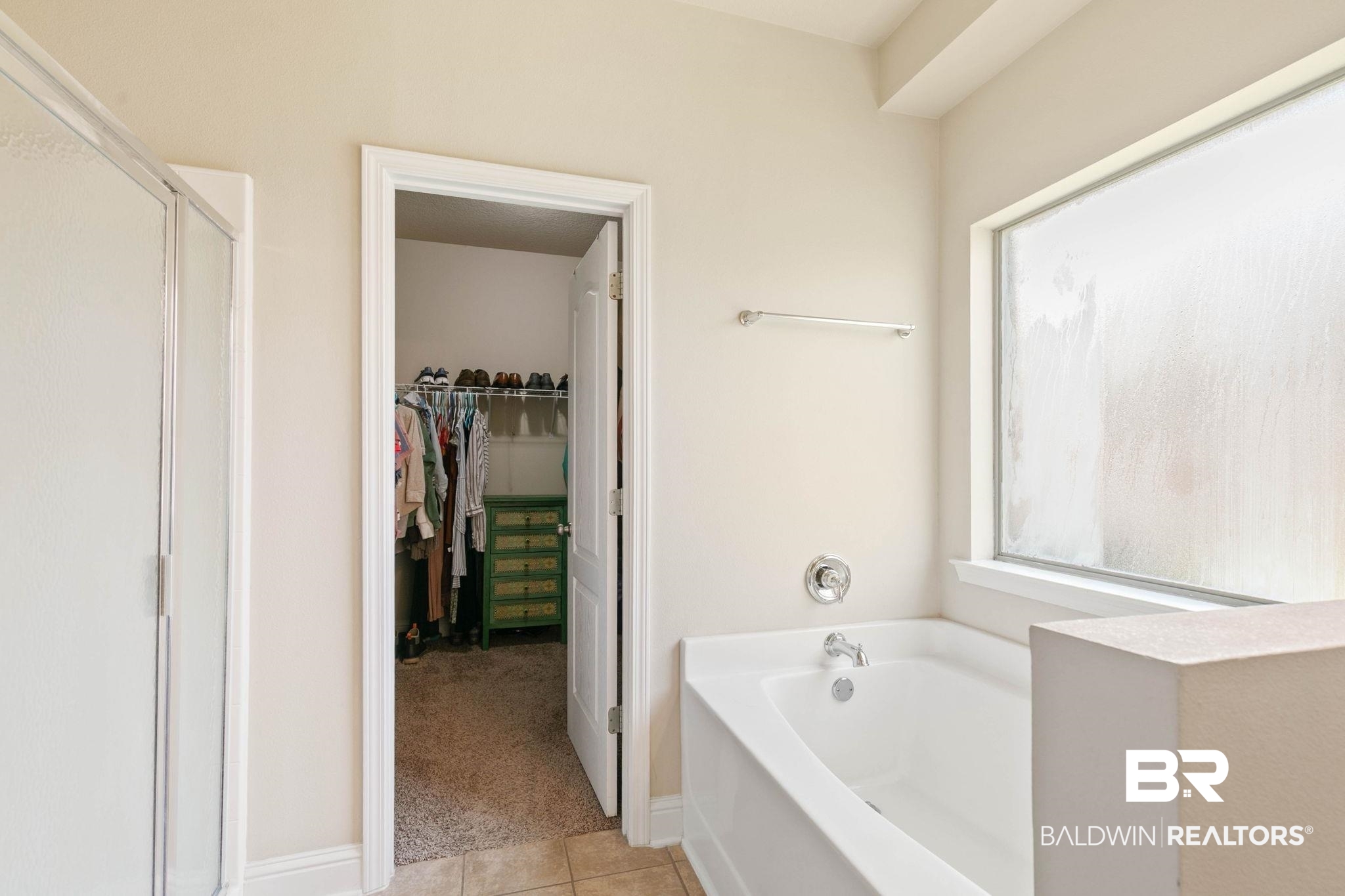 2216 Livingstone Court Mobile, AL 36695 - Photo 25 of 62 Soaking tub with chrome fixtures, frosted glass window, and an adjacent walk-in closet