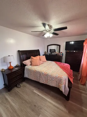 a bedroom with a bed ceiling fan and a wooden floor