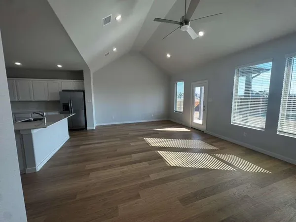 an empty room with wooden floor and a kitchen