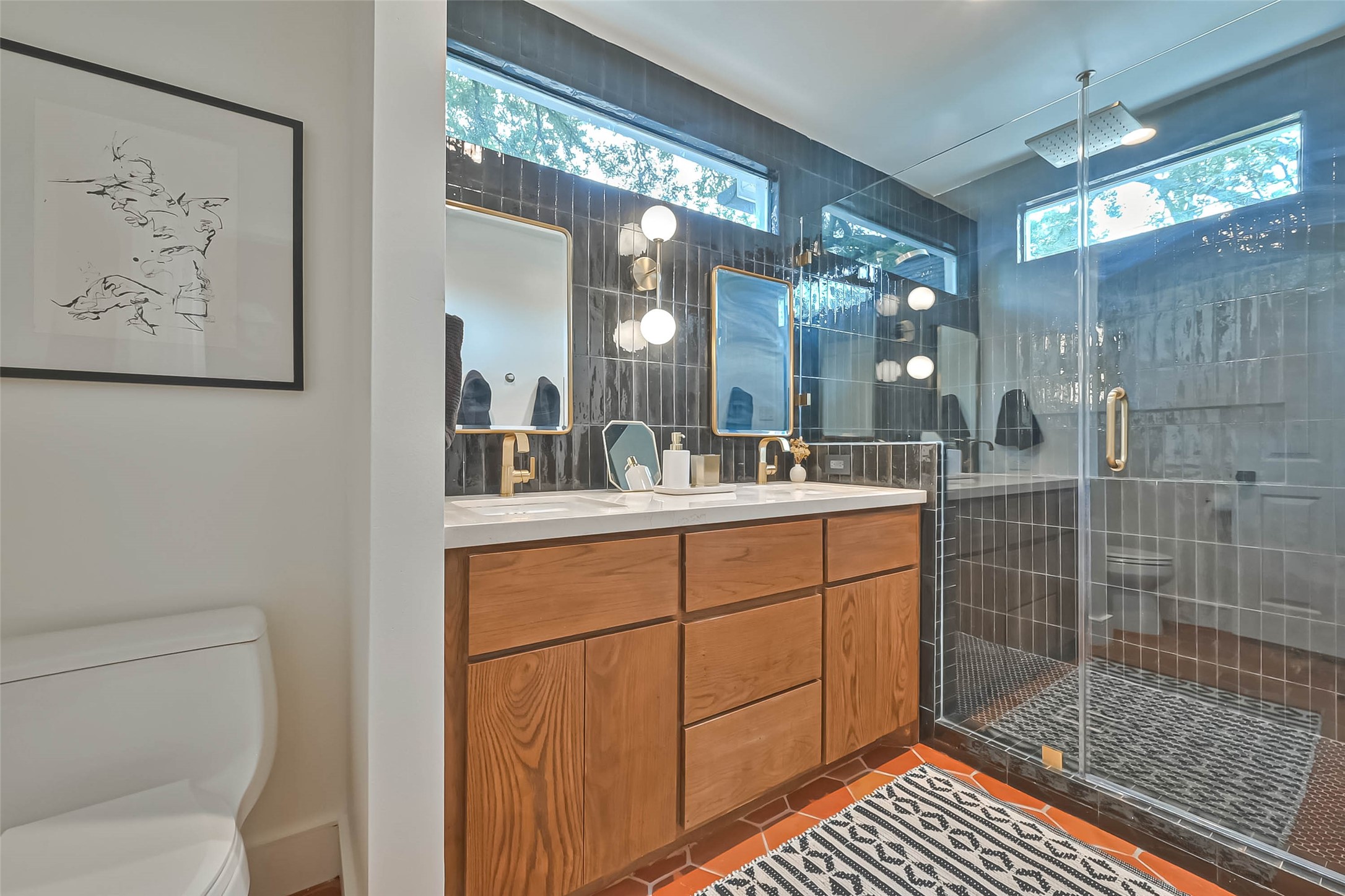 412 Sue Street Houston, TX 77009 - Photo 11 of 19 This primary en suite modern bathroom features a sleek glass-enclosed shower, dual sinks with wooden cabinetry, and stylish black tiles. Natural light filters through high windows, enhancing the contemporary design.