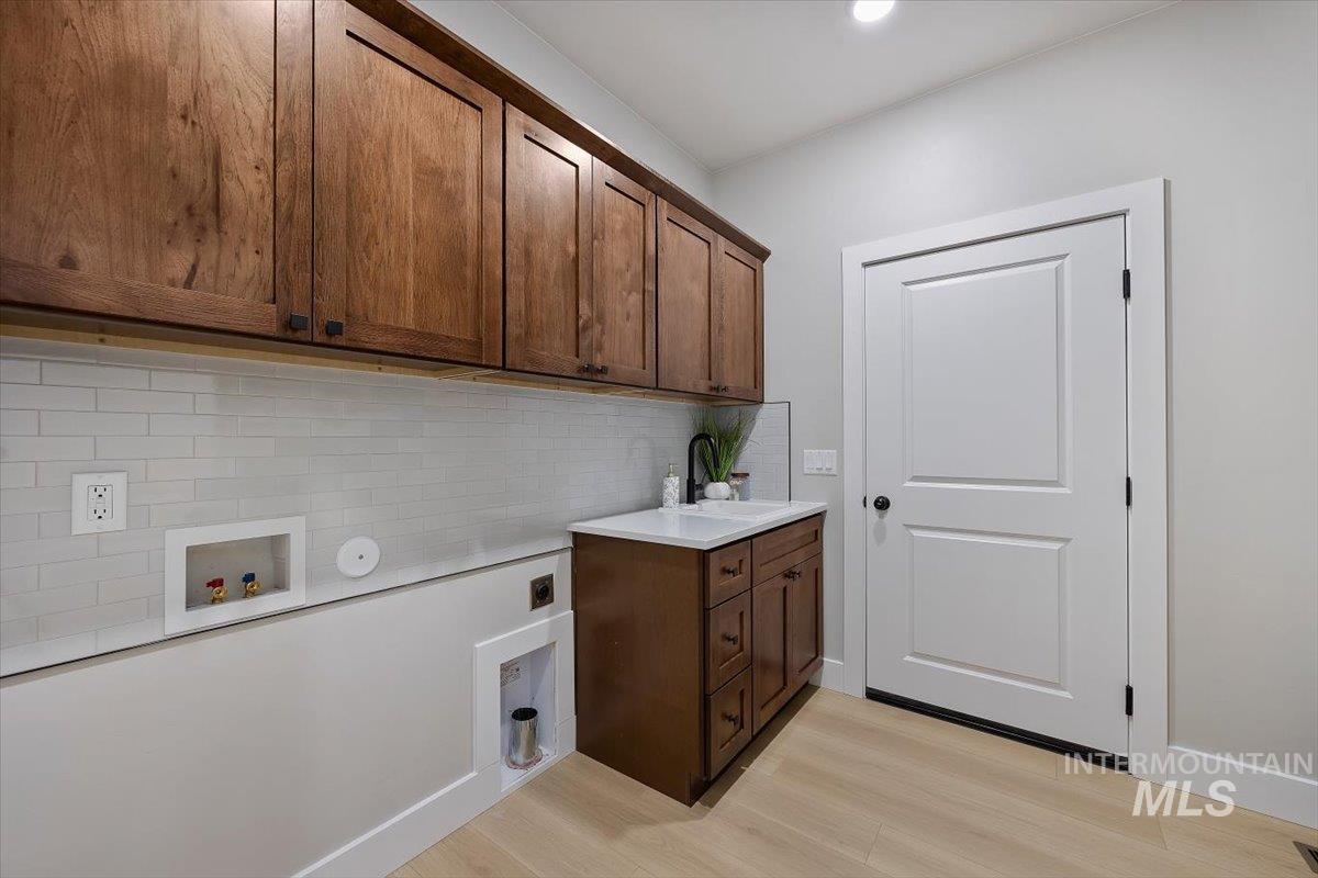 1201 Jade Drive Rupert, ID 83350 - Photo 24 of 27 Functional utility space featuring wood-finish cabinetry, subway tile backsplash, and light wood-finish flooring