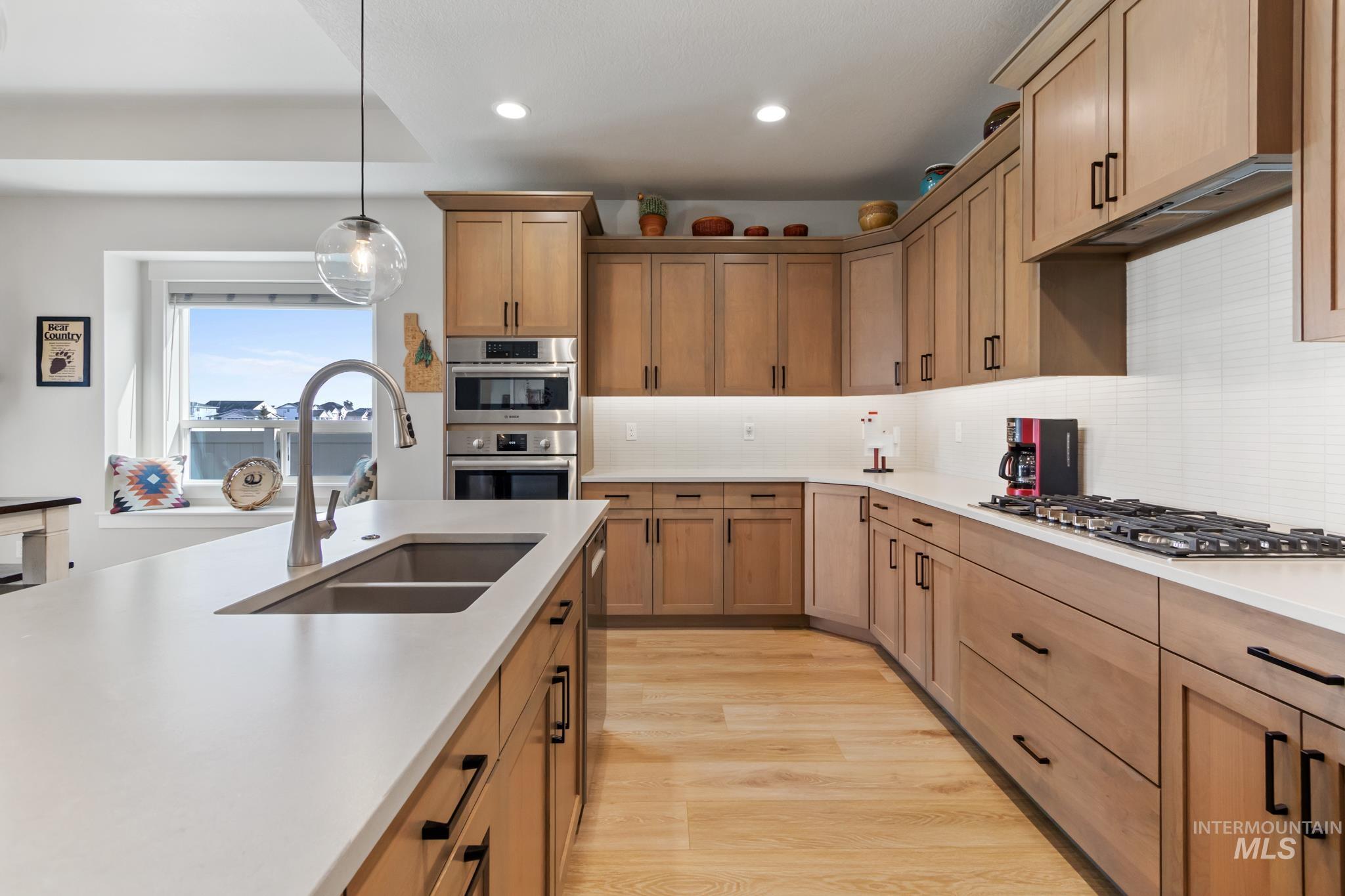 9864 West Aviara Street Star, ID 83669 - Photo 15 of 40 Kitchen with decorative light fixtures, light wood-style flooring, backsplash, wood finish cabinetry, and stainless steel appliances