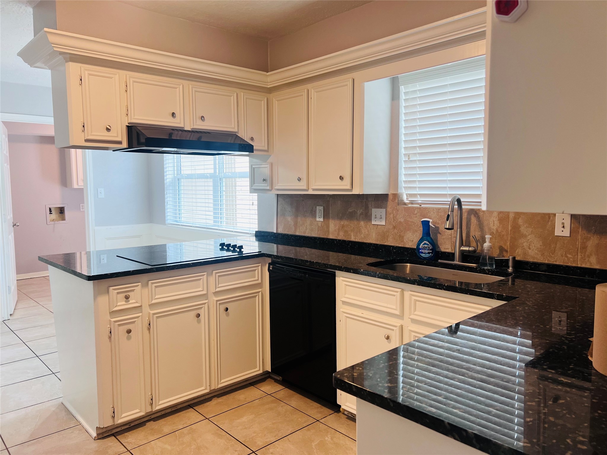902 Hidden Canyon Road Katy, TX 77450 - Photo 5 of 20 This kitchen features elegant black granite countertops, white cabinetry, and a built-in stovetop. Natural light streams in through a window above the sink, creating a bright and inviting space.