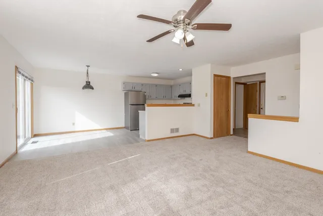 an empty room with a ceiling fan and a kitchen view