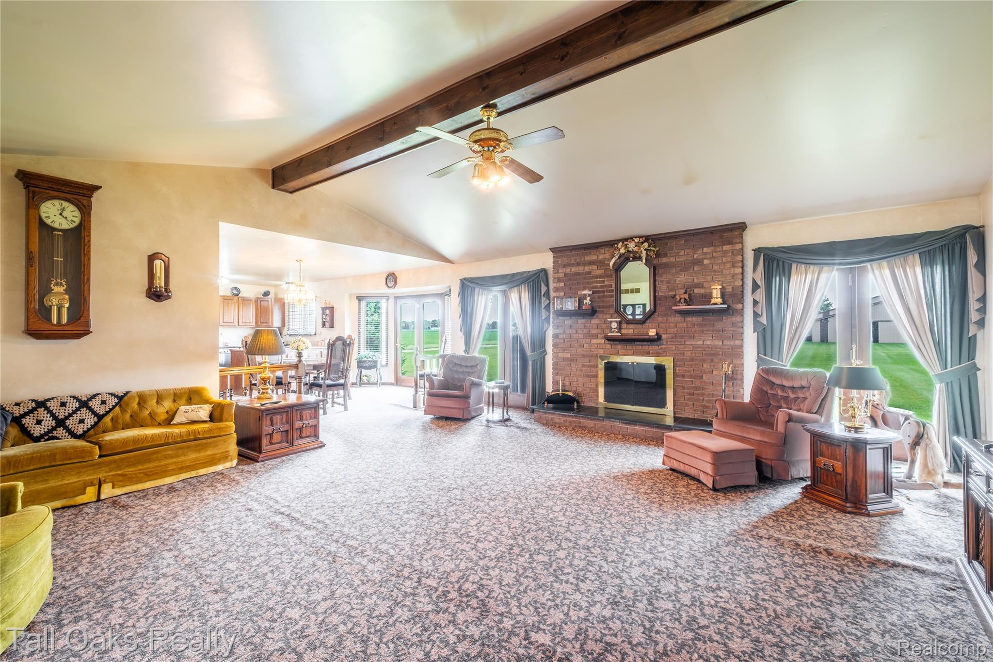 79330 Capac Road Armada, MI 48005 - Photo 28 of 42 Spacious living area featuring a brick fireplace with a brass-trimmed insert, vaulted ceiling with exposed wood beams, and a ceiling fan