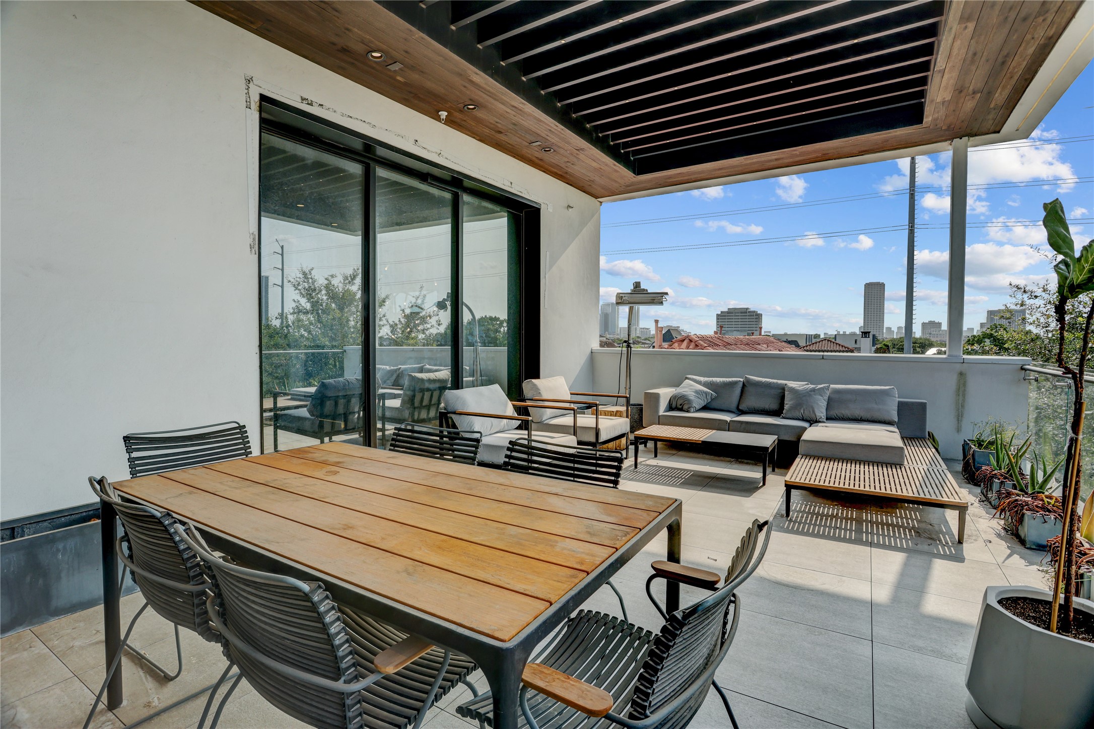 1807 Indiana Street Houston, TX 77006 - Photo 33 of 35 Rooftop Terrace Overview: Comprehensive view of the top-floor deck looking back at the large sliding glass doors, highlighting the distinct outdoor dining and lounge zones, modern louvered patio ceiling structure, and sweeping urban views.