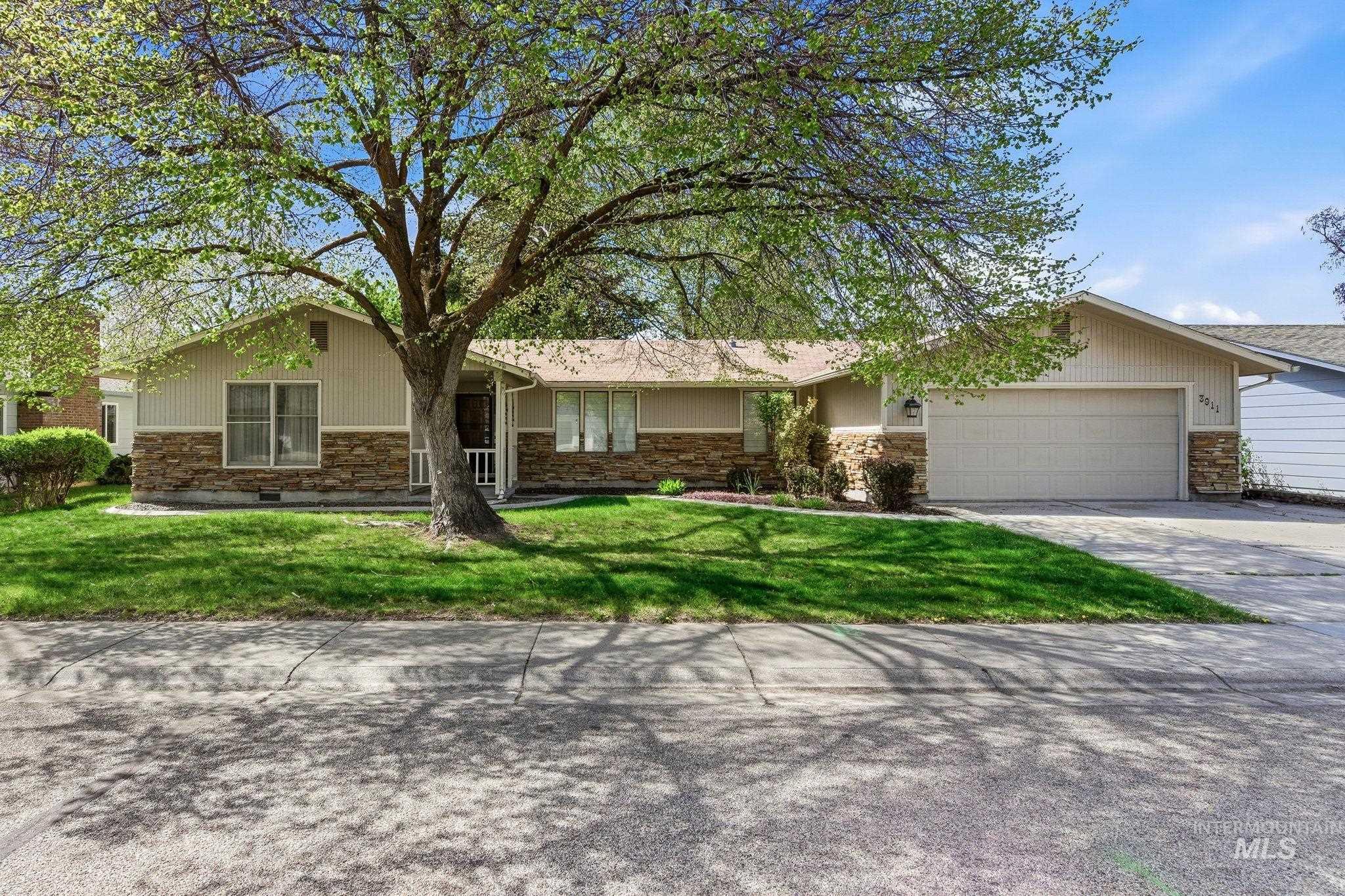 Ranch-style home featuring an attached garage, concrete driveway, a front lawn, and stone siding
