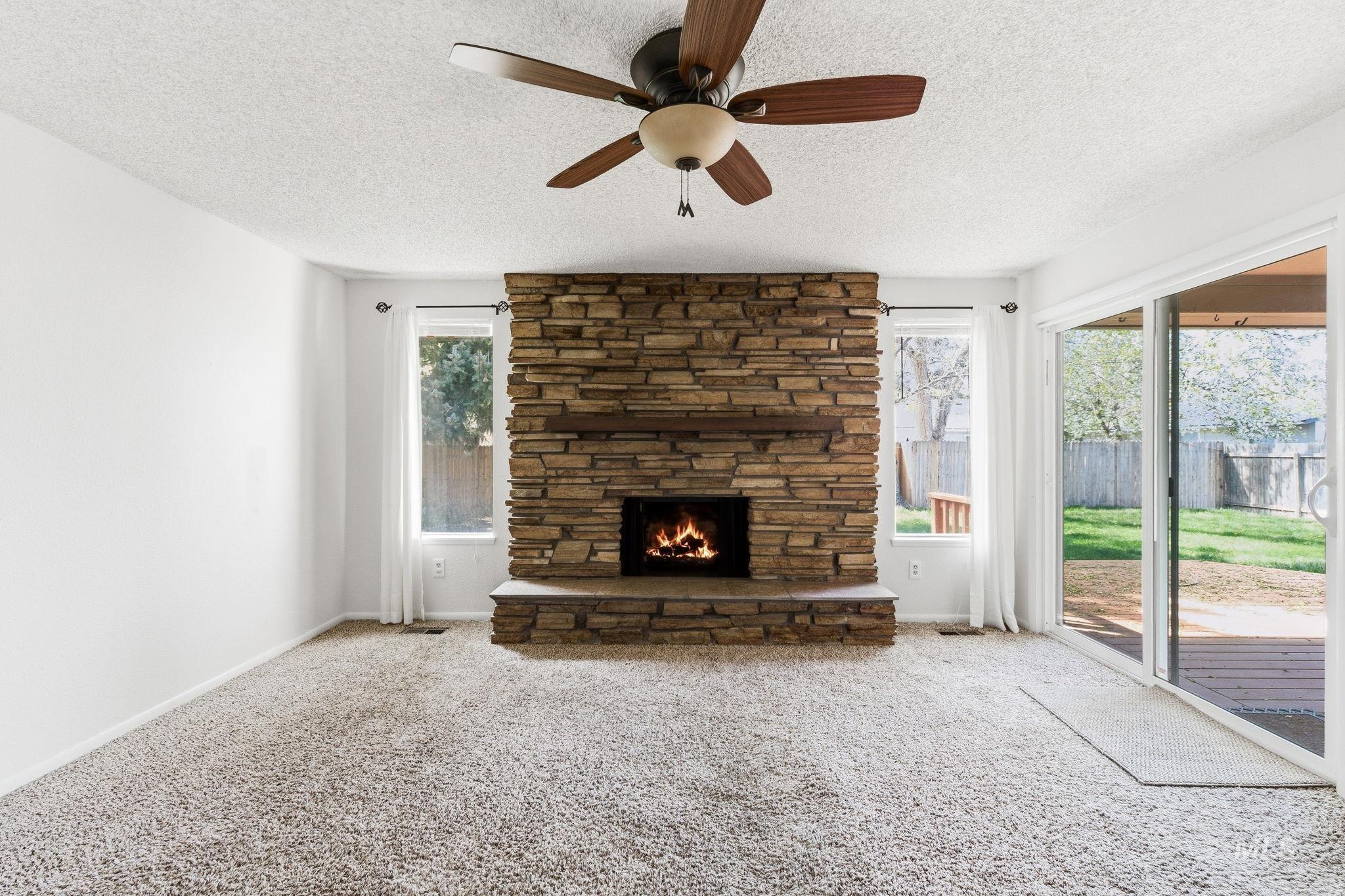 3911 South Constitution Way Boise, ID 83706 - Photo 11 of 40 Unfurnished living room with ceiling fan, a stone fireplace, carpet floors, and a textured ceiling