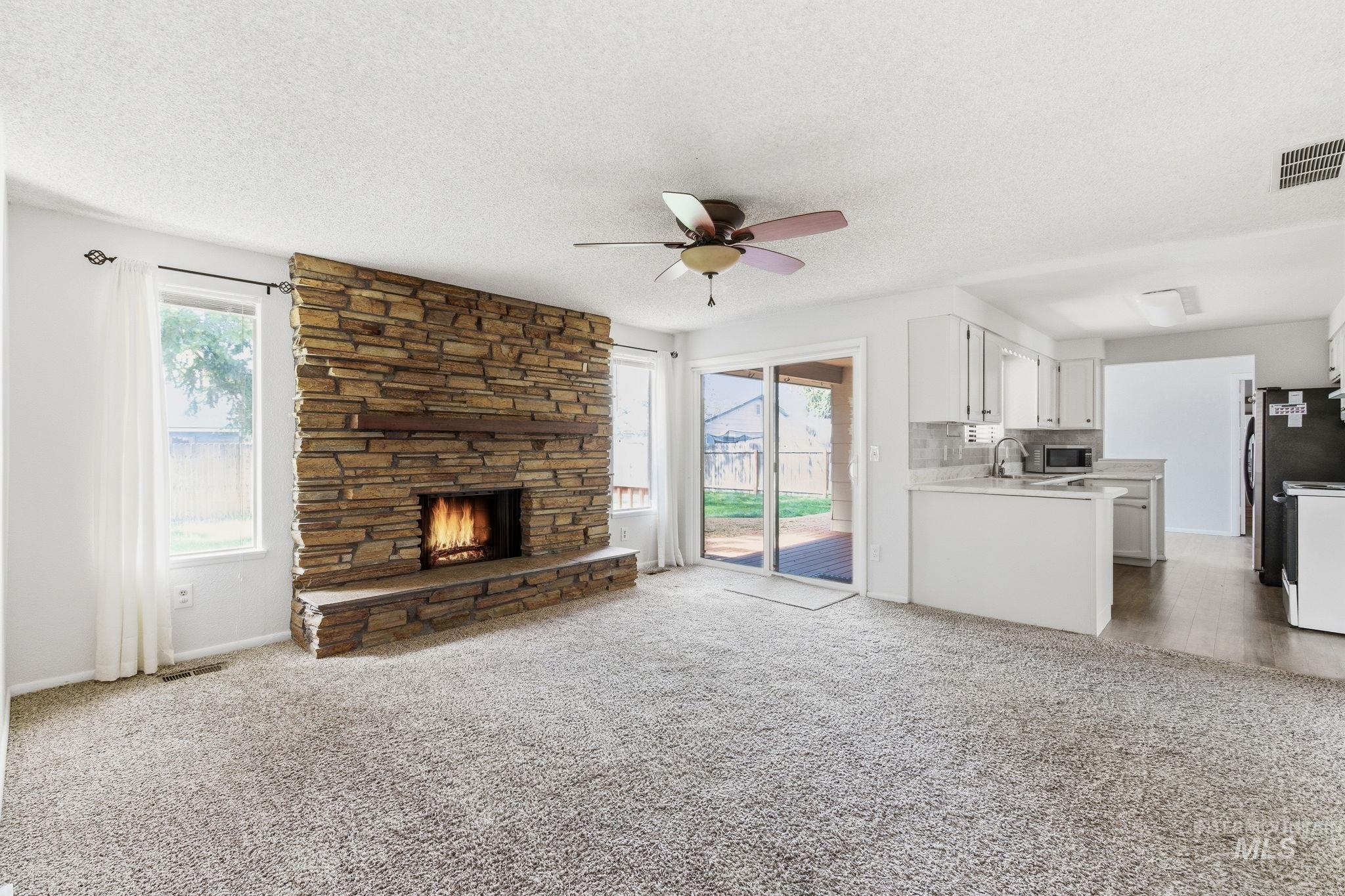 3911 South Constitution Way Boise, ID 83706 - Photo 12 of 40 Unfurnished living room with a ceiling fan, light colored carpet, a fireplace, a textured ceiling, and plenty of natural light