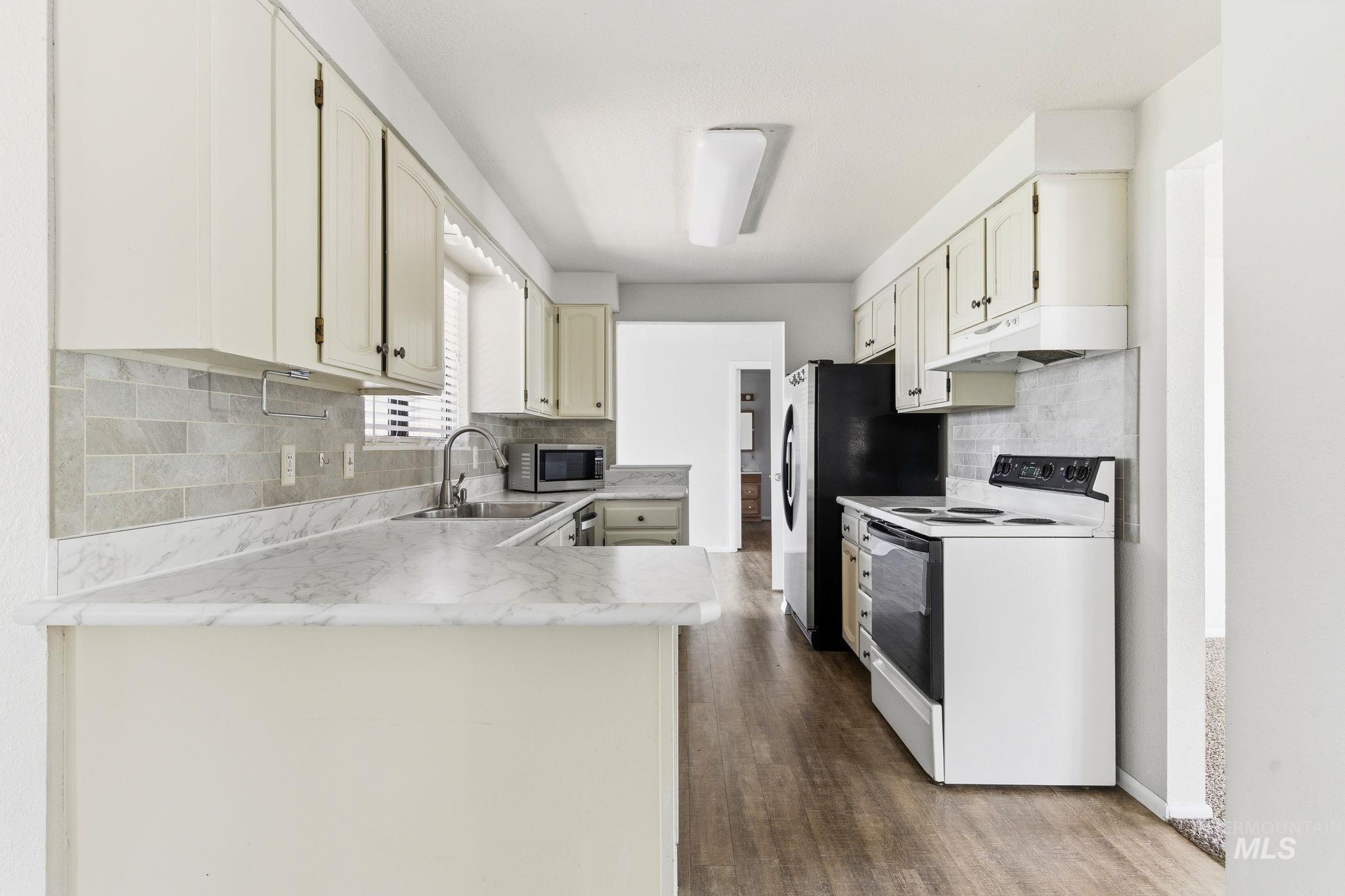 3911 South Constitution Way Boise, ID 83706 - Photo 13 of 40 Kitchen with light countertops, stainless steel appliances, dark wood-style floors, decorative backsplash, and a peninsula