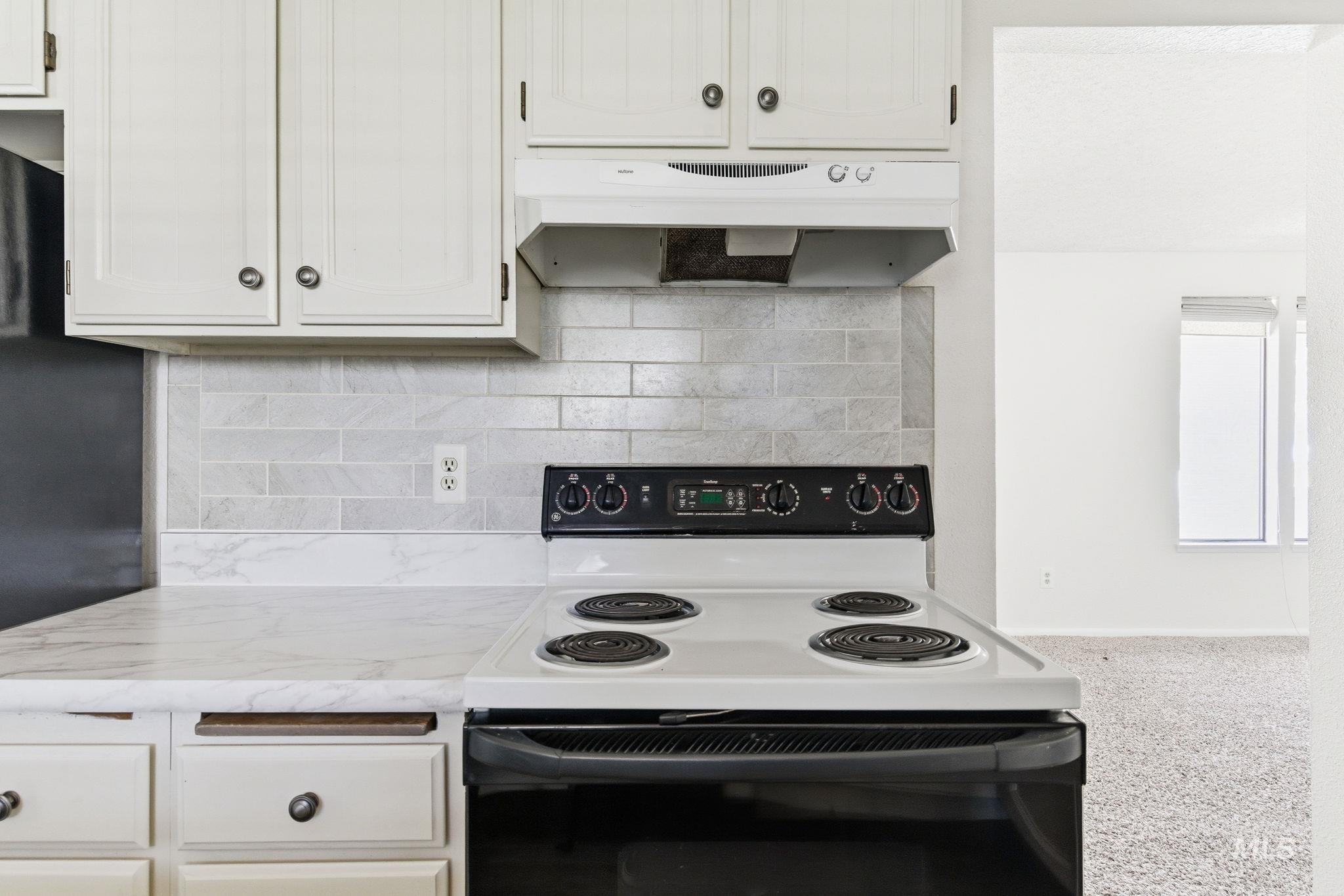 3911 South Constitution Way Boise, ID 83706 - Photo 16 of 40 Kitchen featuring electric range, light countertops, ventilation hood, backsplash, and white cabinets