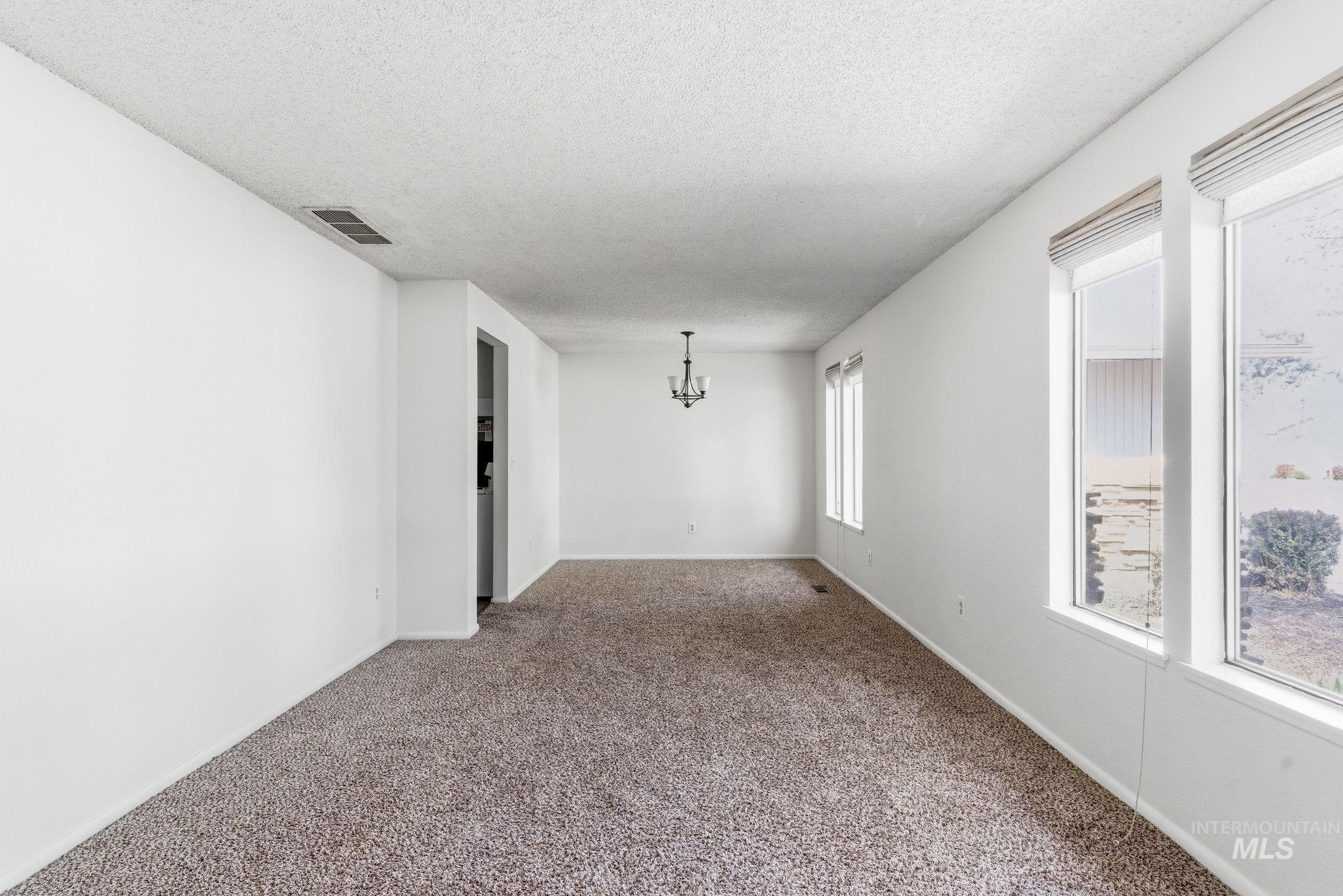 3911 South Constitution Way Boise, ID 83706 - Photo 6 of 40 Carpeted empty room with a chandelier and a textured ceiling