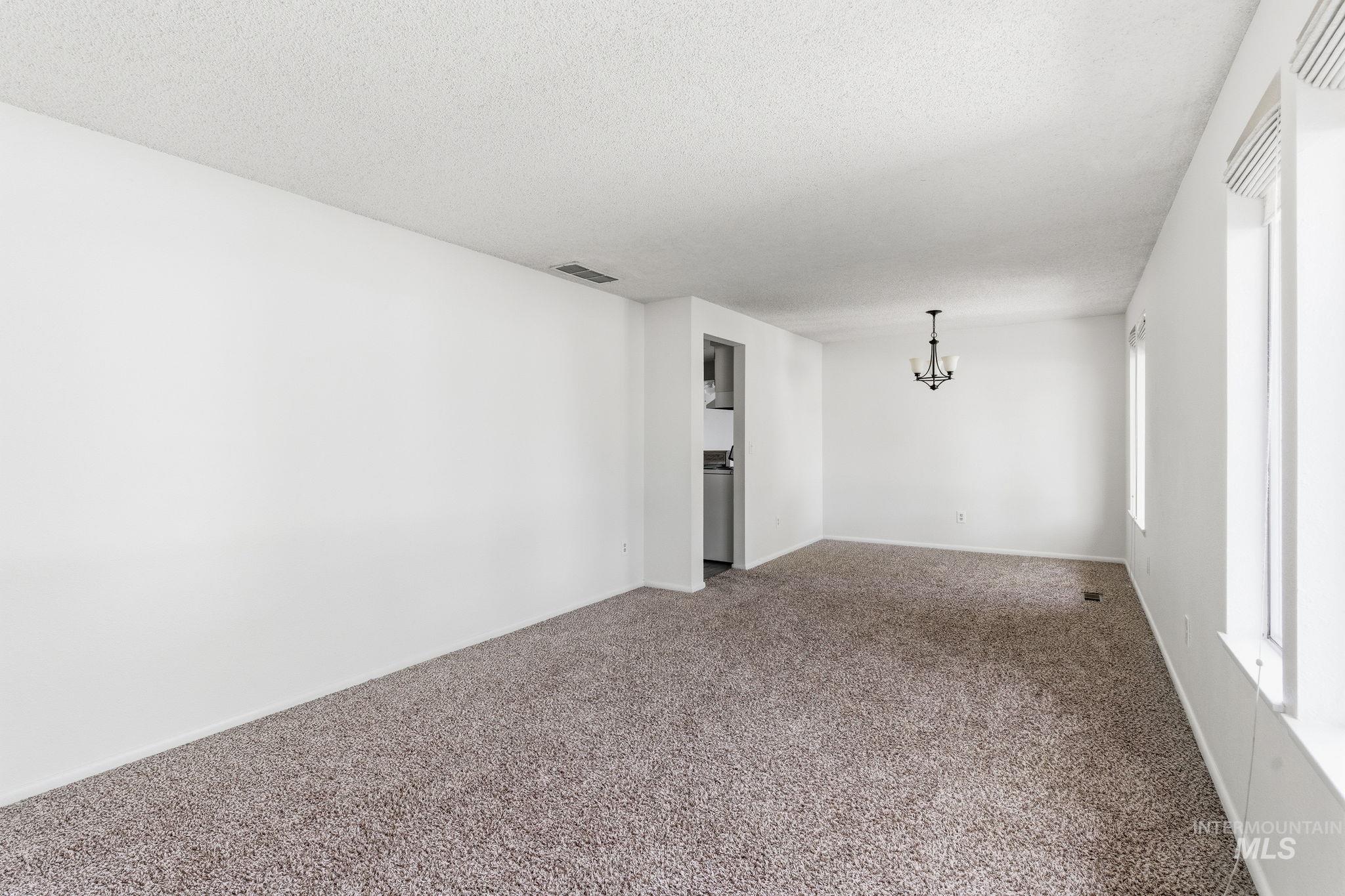3911 South Constitution Way Boise, ID 83706 - Photo 7 of 40 Spare room with carpet floors, a chandelier, and a textured ceiling