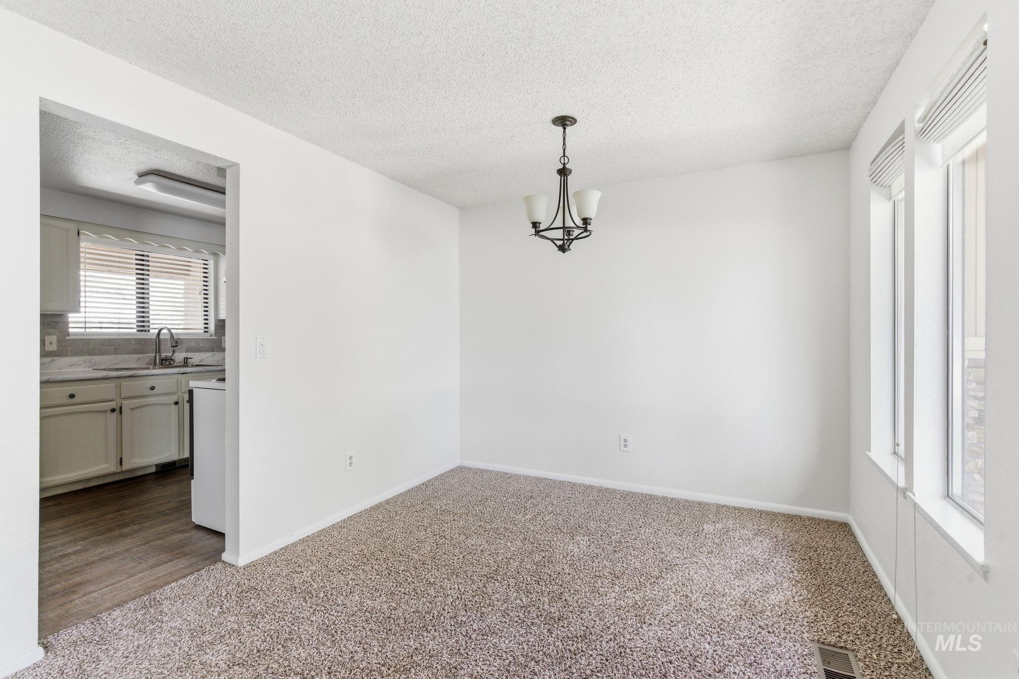 3911 South Constitution Way Boise, ID 83706 - Photo 9 of 40 Unfurnished dining area with dark carpet, a textured ceiling, and a chandelier