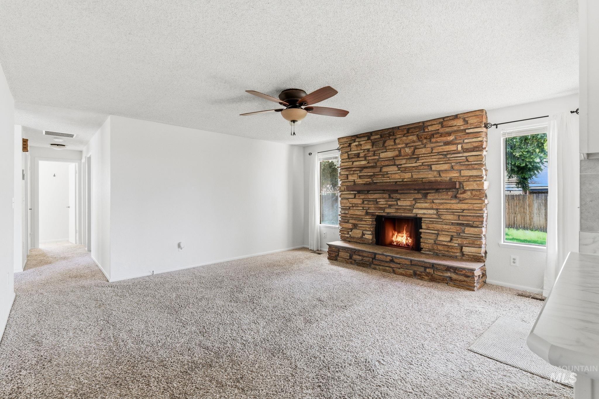 3911 South Constitution Way Boise, ID 83706 - Photo 10 of 40 Unfurnished living room featuring light carpet, a ceiling fan, a fireplace, and a textured ceiling