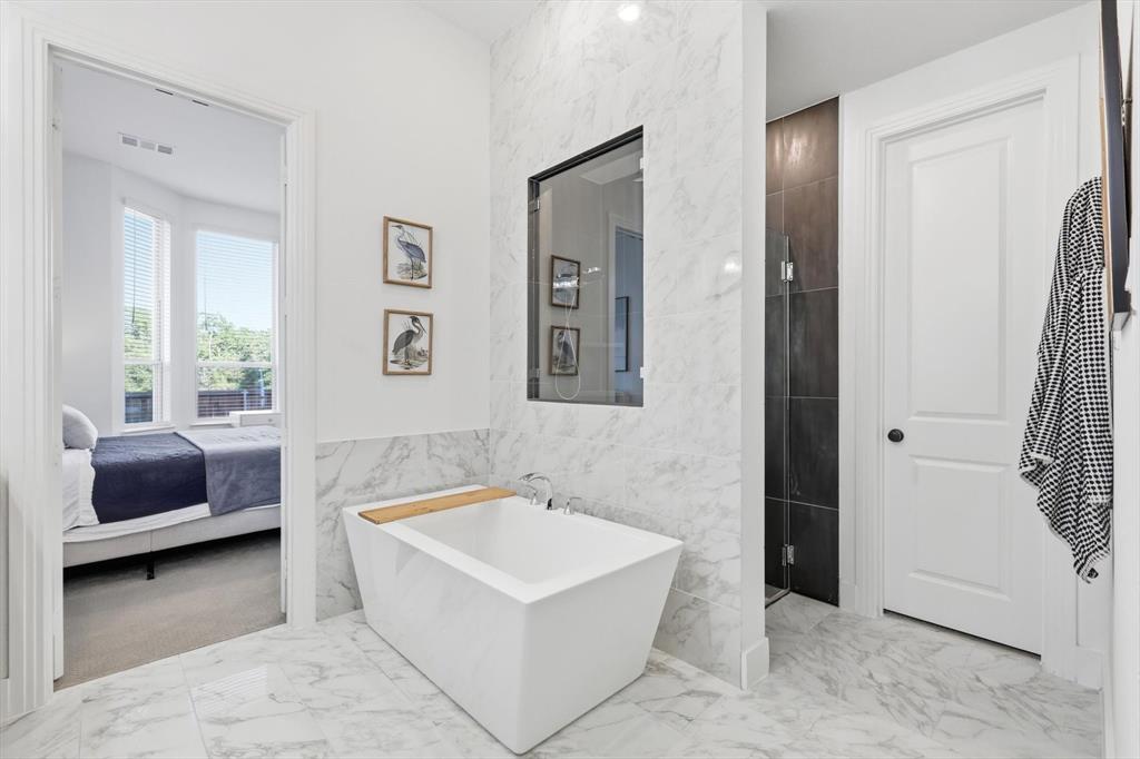 4608 Mount Vista Road Oak Point, TX 75068 - Photo 29 of 39 Freestanding soaking tub with a wood-finish caddy, marble-look floor tile, marble-look wall tiling, and a frameless glass shower enclosure with dark tile surround