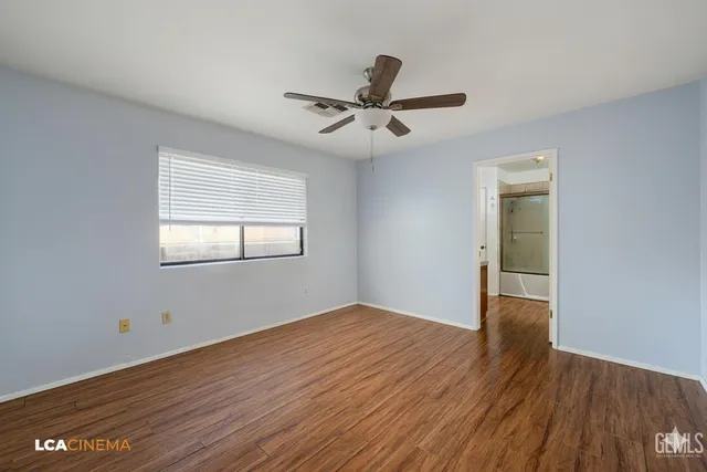 an empty room with wooden floor a ceiling fan and windows