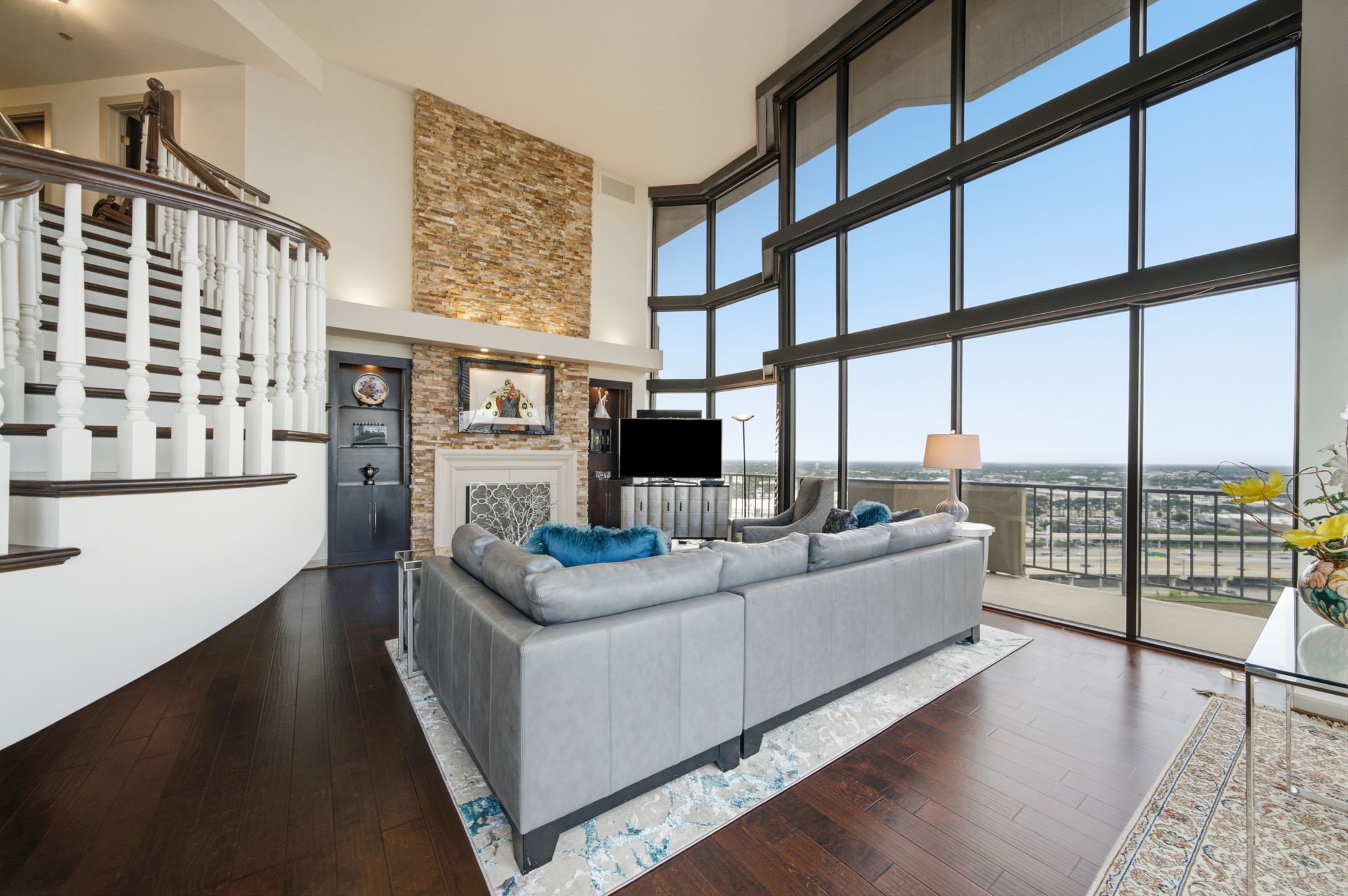 3350 McCue Road, Unit 2402 Houston, TX 77056 - Photo 16 of 49 Soaring double-height glass walls frame endless horizon vistas in this magnificent grand salon. A towering stacked-stone fireplace with custom built-in display niches commands attention alongside the curved staircase and rich hardwood flooring.