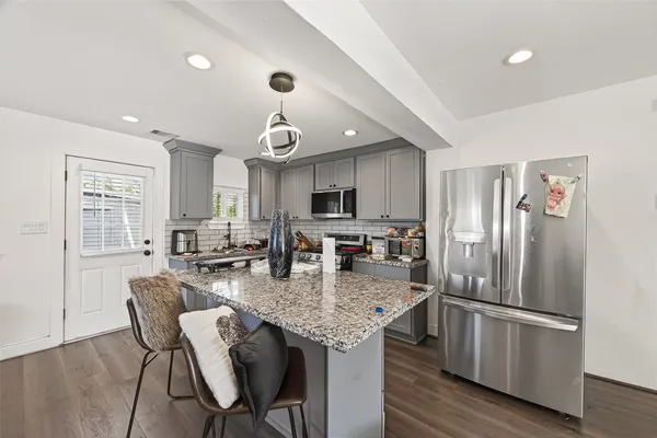 a kitchen with stainless steel appliances granite countertop a stove a refrigerator a kitchen island a sink dishwasher and white cabinets with wooden floor