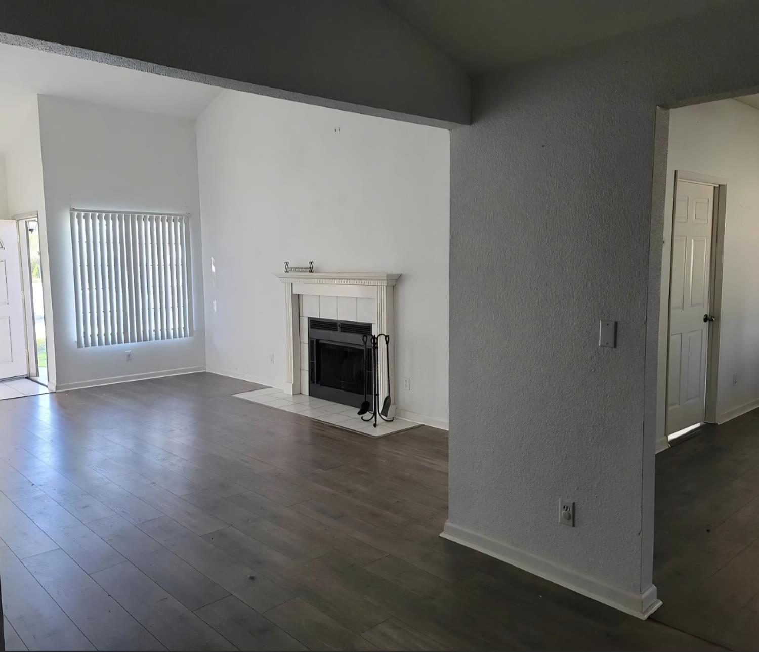 an empty room with wooden floor fireplace and windows