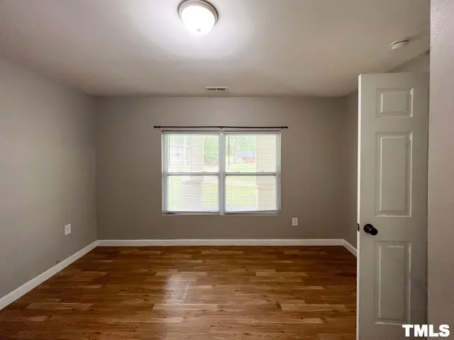 a view of an empty room with window and wooden floor