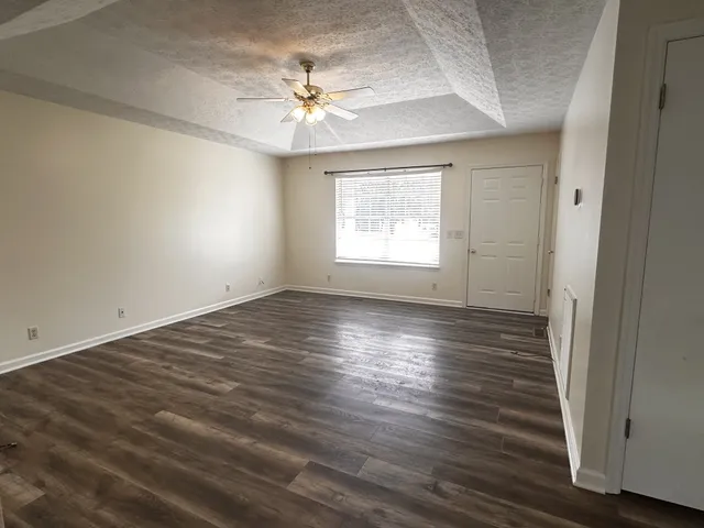 an empty room with wooden floor chandelier fan and windows