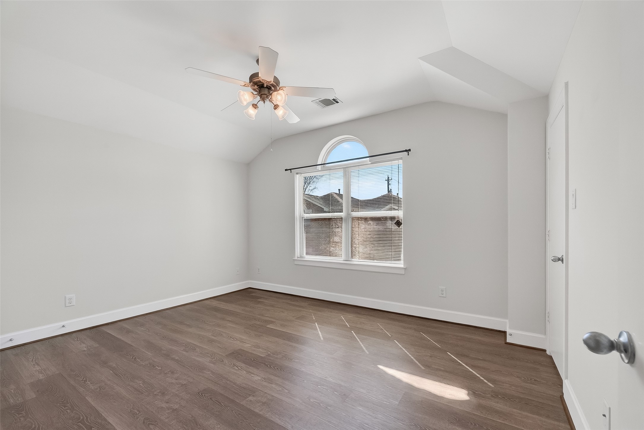 5951 S Loop East, Unit 47 Houston, TX 77033 - Photo 25 of 37 Bright and spacious Guest bedroom with vaulted ceiling, modern ceiling fan, and large window for ample natural light. Features sleek hardwood flooring and neutral walls, creating a fresh and inviting atmosphere.