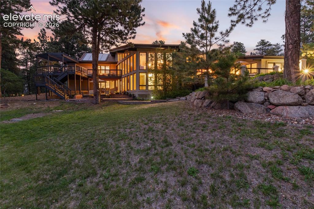 12730 Bridle Bit Road Colorado Springs, CO 80908 - Photo 46 of 50 Contemporary multi-level residence featuring extensive window walls, multiple outdoor decks, a stone retaining wall, and mature trees