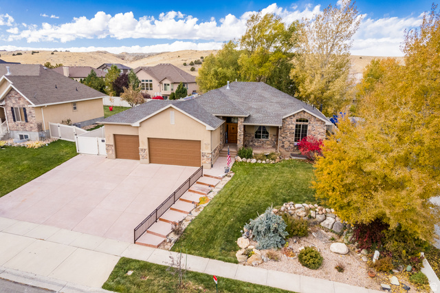 Ranch-style home with an attached garage, stone siding, driveway, a gate, and stucco siding