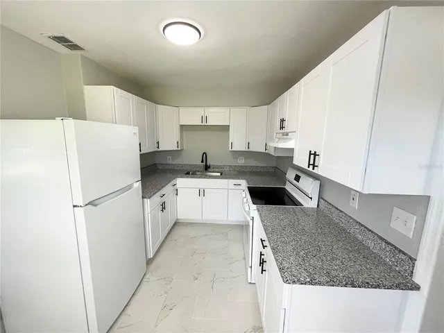 a kitchen that has a refrigerator a stove a sink and white cabinets