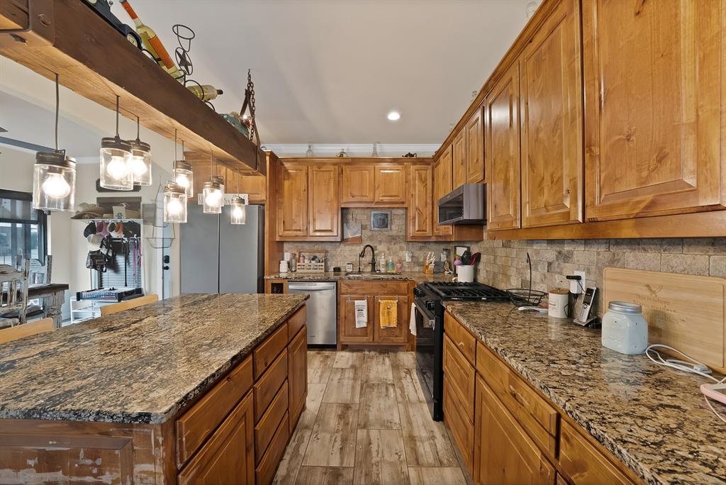 100 Shadle Ridge Court Poolville, TX 76487 - Photo 9 of 40 Kitchen featuring wood-finish cabinetry, granite countertops, tile backsplash, stainless steel appliances, and a central island with pendant lighting