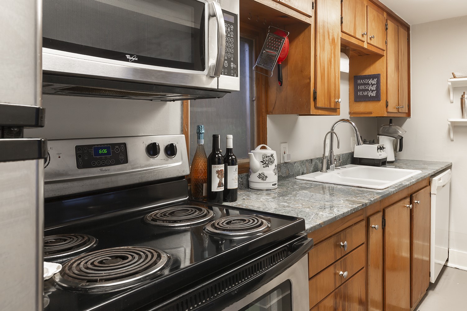 1209 Bomar Street Houston, TX 77006 - Photo 16 of 23 Guest house kitchen features stainless steel appliances, wooden cabinetry, and a granite countertop. It includes an electric stove, microwave, sink, and dishwasher, offering a functional and cozy cooking space.