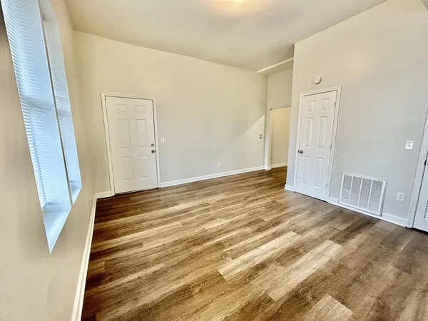a view of an empty room with wooden floor and a bathroom