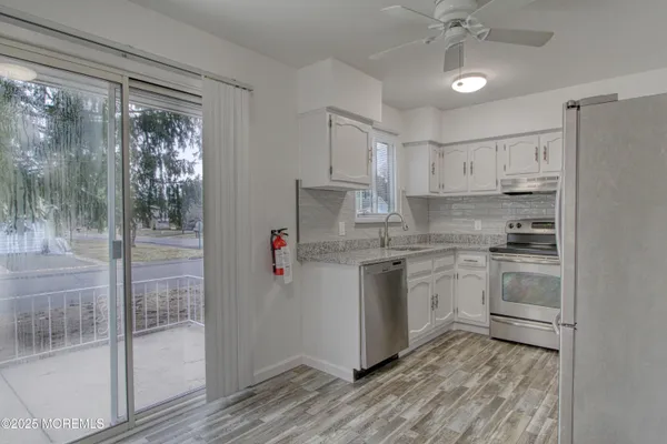 a kitchen with stainless steel appliances granite countertop a refrigerator a sink a stove and white cabinets with wooden floor