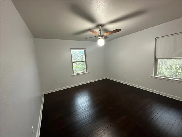 an empty room with wooden floor fan and windows