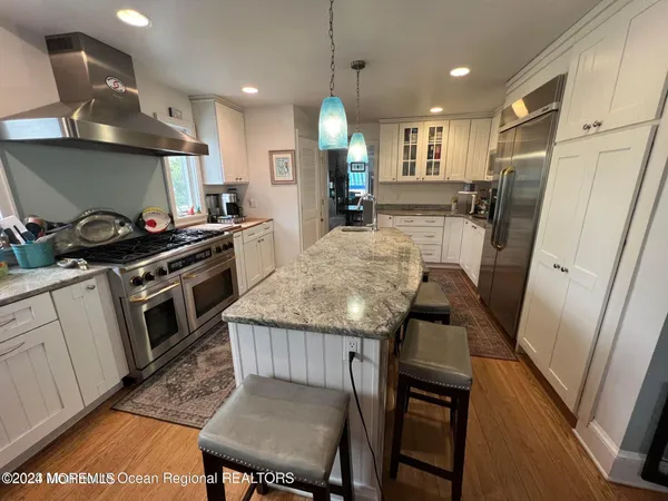 a kitchen with granite countertop a stove a sink a refrigerator wooden floor and cabinets