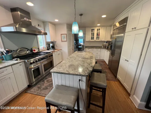 a kitchen with granite countertop a stove a sink a refrigerator wooden floor and cabinets