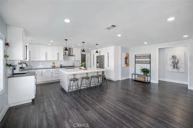 a living room with stainless steel appliances furniture wooden floor and a kitchen view